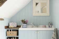 a small powder blue attic bathroom with wooden beams, baskets for storage and a free-standing tub