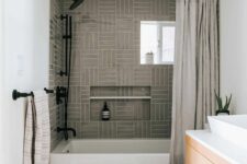 a small yet chic bathroom with grey stacked tiles, a bathtub, a stained vanity, a bold printed rug and a potted plant
