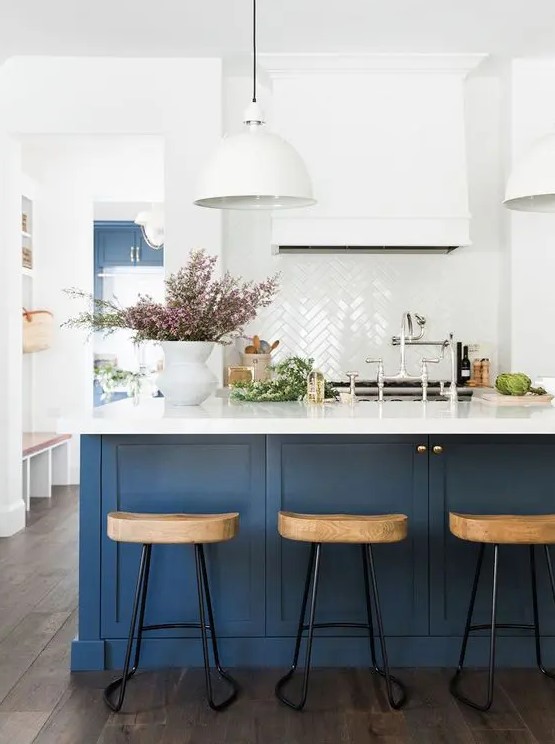 a sophisticated navy and white kitchen with shaker cabinets and a storage kitchen island, a white herringbone tile backsplash and wooden stools