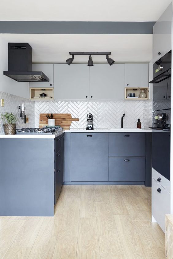 a stylish IKEA kitchen with light grey and navy cabinets, a white herringbone tile backsplash and white countertops and black touches