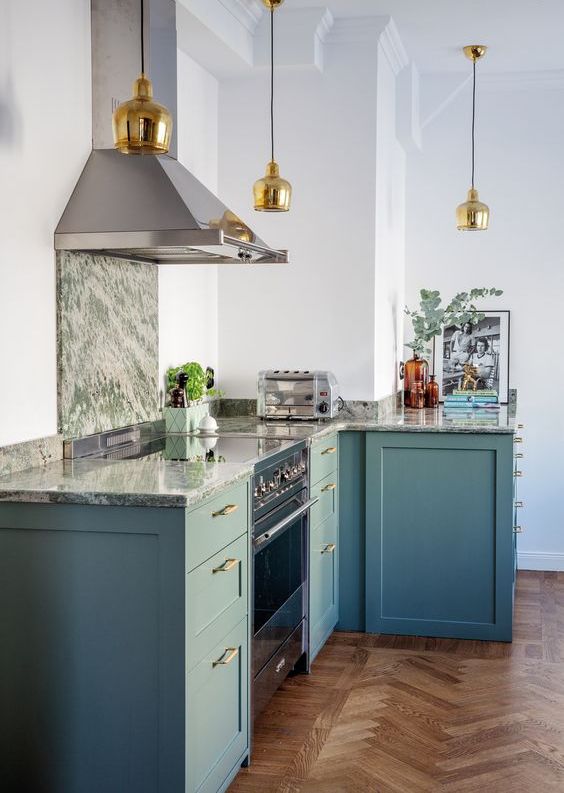 a stylish blue kitchen with only lower cabinets, a grey stone countertop and backsplash, gold pendant lamps and handles
