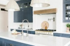 a stylish farmhouse kitchen in an elegant blue shade, with white stone countertops, a white backsplash and pendant lamps