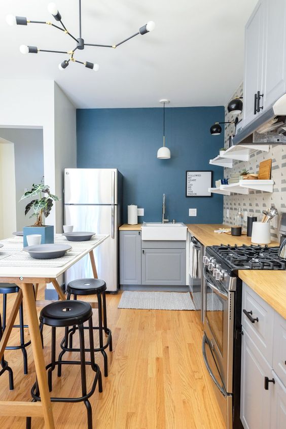 a stylish grey IKEA kitchen with a navy accent wall, open shelves, butcherblock countertops, a tall table that doubles as a kitchen island and stools