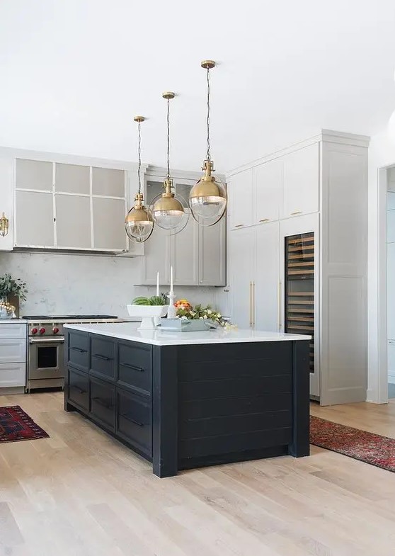 a stylish kitchen with white and dove grey cabinets, a midnight blue kitchen island, elegant gold pendant lamps
