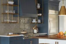 a stylish modern kitchen with blue shaker cabinets and a grey subway tile backsplash, suspended shelves, a kitchen island and brass touches