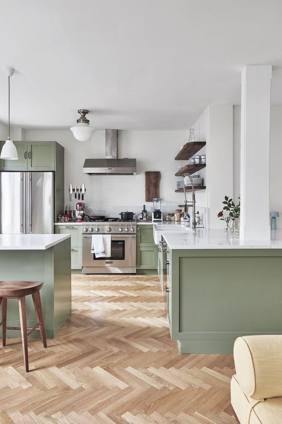 a stylish modern kitchen with green cabinets and white countertops, a kitchen island, stained shelves and stools and some lamps