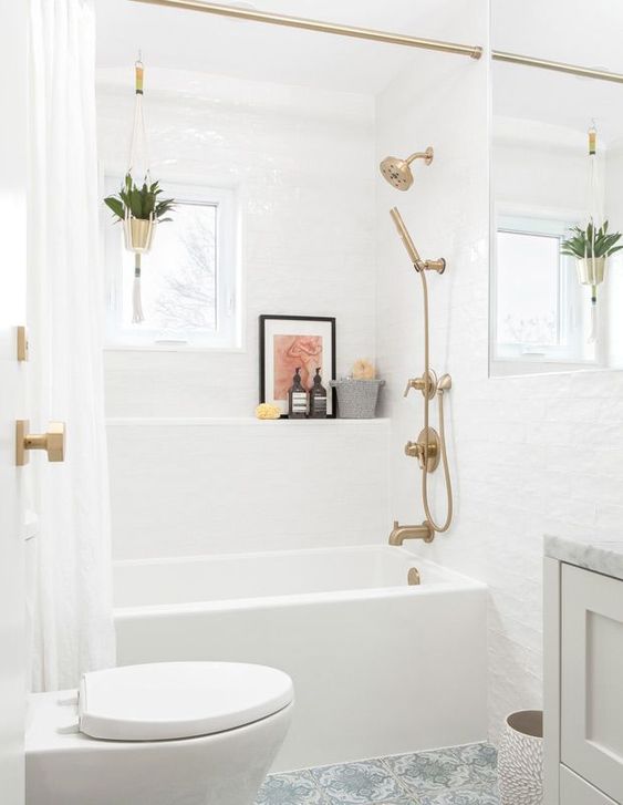 a stylish neutral bathroom with a tub and a shelf over it, a white vanity, a toilet and brass fixtures