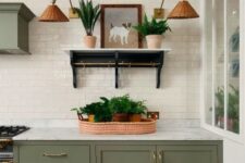 a stylish olive green farmhouse kitchen with shaker cabinets, a matching hood, a white subway tile backsplash, an open shelf, woven sconces