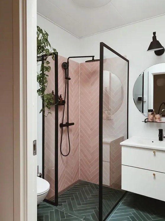 a stylish small bathroom with green herringbone tiles on the floor, pink ones in the shower, a floating vanity and black framing