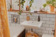 a tiny and cozy boho bathroom with white tiles, a bathtub clad with wood, a wall-mounted sink and a shelf, potted greenery