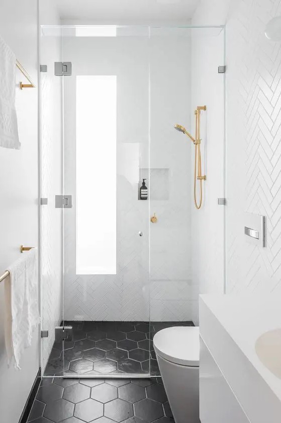 a tiny black and white bathroom with white herringbone tiles on the walls, black hexagon ones on the floor and gold fixtures