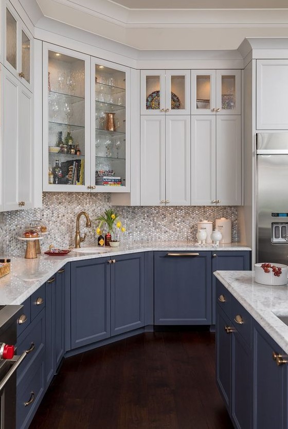 a traditional kitchen with blue lower cabinets, neutral upper ones, a mother of pearl bacskplash and touches of gold
