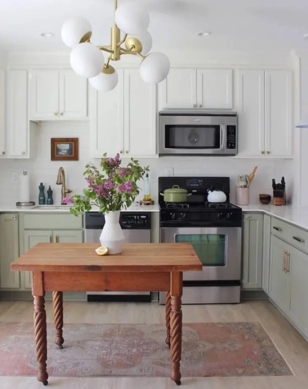 a two-tone kitchen with white and sage green cabinets, a white tile backsplash and countertops and a small table as a kitchen island
