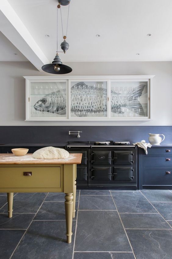 a unique kitchen with an ocean blue wall and matching cabinets, a large vintage cooker, a yellow table and kitchen island, pendant lamps and a bold artwork