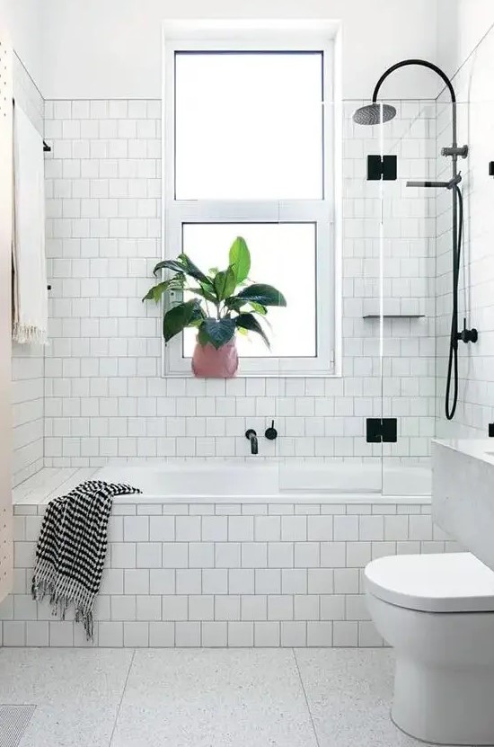 a white Scandinavian bathroom done with square tiles, a tub clad with tiles, black fixtures and a floating vanity