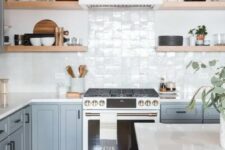 an airy kitchen with light blue cabinets, a white Zellige tile backsplsh, open shelves and white countertops