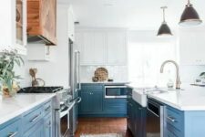 an airy kitchen with white and blue cabinets, white quartz countertops, a white backsplash and stainless steel handles plus a stained wooden hood