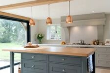 an elegant kitchen with grey cabinets, a large grey hood, a navy kitchen island with a butcheblock countertop and copper pendant lamps