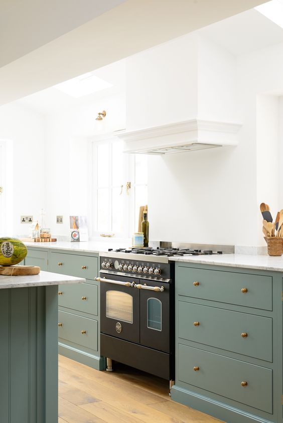 an elegant kitchen with white walls and green cabinets, a matching kitchen island, a white hood and a black cooker