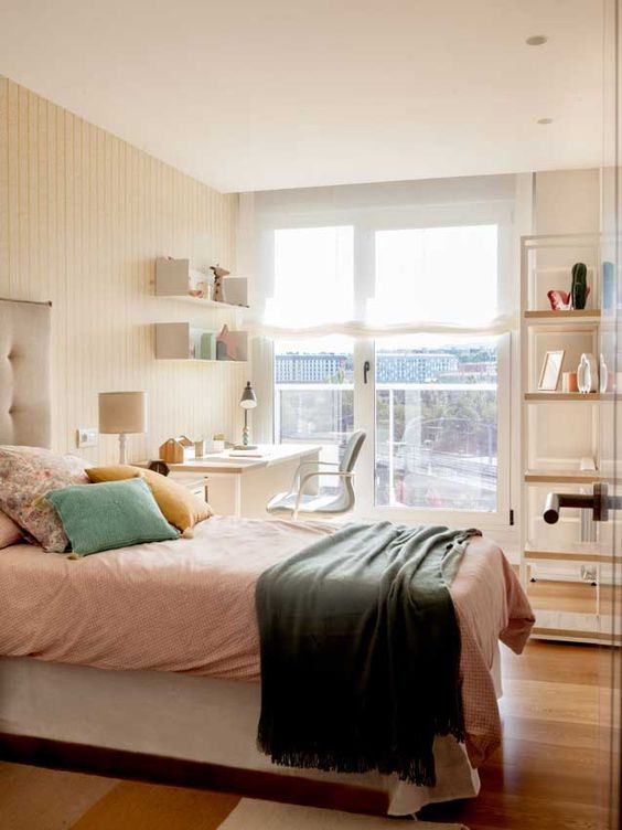 an airy guest bedroom with a desk and open shelves, a comfy bed with pillows and lots of natural light
