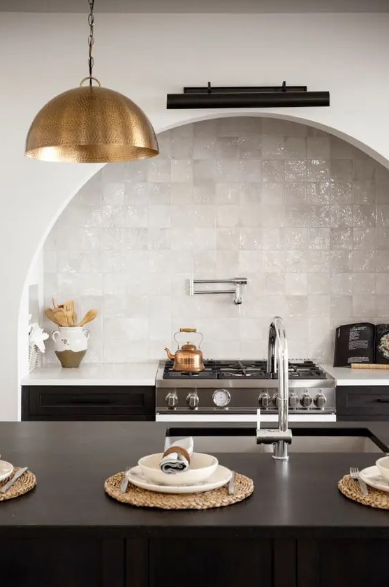 a chic kitchen with a black kitchen island and cabinets, an arched niche over the cooker with a built-in hood and white Zellige tiles