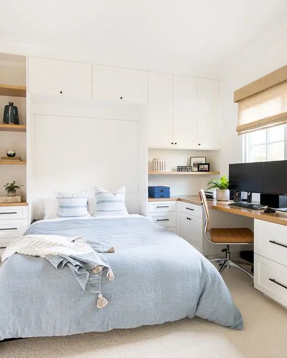 a white guest bedroom with a Murphy's bed, open shelves, a desk, a tan chair and some shades