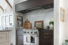05 a modern farmhouse kitchen in white, with a large niche with dark-stained cabinets and a hood, some small shelves for condiments and oils