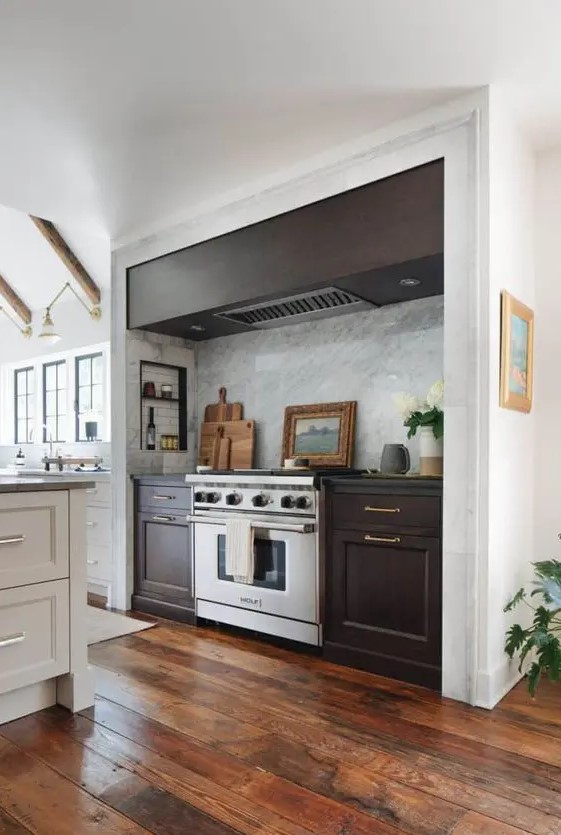 a modern farmhouse kitchen in white, with a large niche with dark-stained cabinets and a hood, some small shelves for condiments and oils