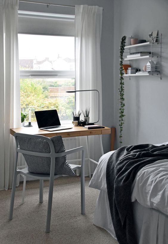 a small IKEA Scandinavian guest bedroom with a large bed, a lightweight stained desk, a grey chair and open shelves