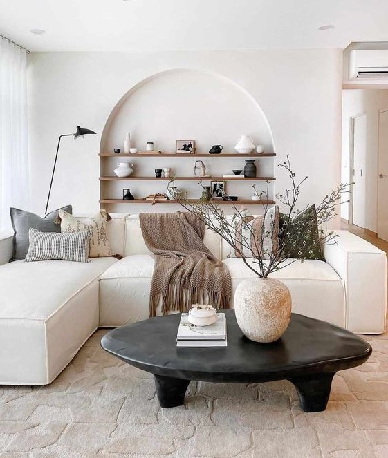 a beautiful minimalist living room in neutrals, with an arched niche with shelves and chic decor, with a low sofa and a black coffee table