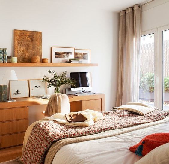 a small guest bedroom with a cool bed, a stained desk, an open shelf and much decor and artwork is a lovely light-filled space