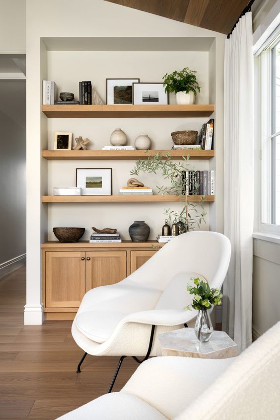 a beautiful nook with niche shelves and built-in cabinets for storage and decor, a creamy Womb chair and some plants