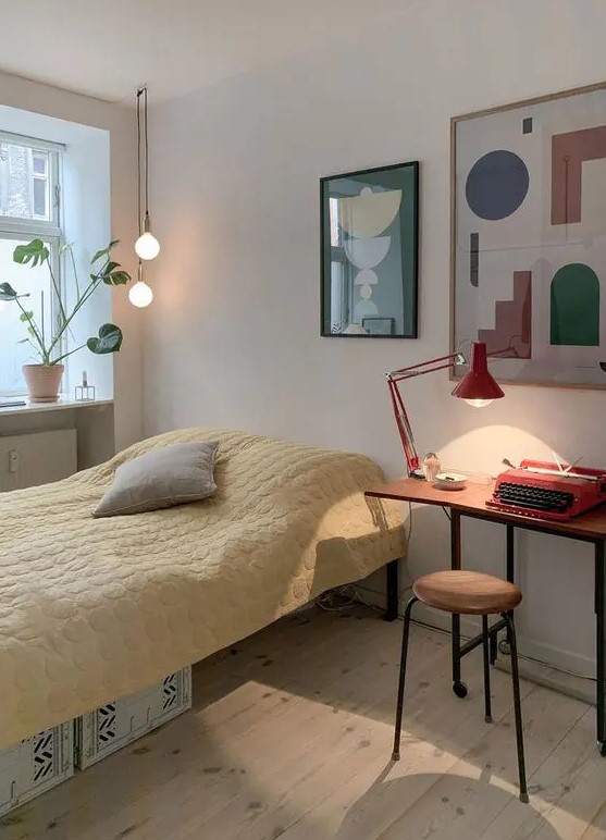 a Scandinavian guest bedroom with a bed with yellow bedding, a small desk, a stool, a mini gallery wall and some cool lamps