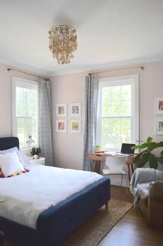 a pretty pink guest bedroom with a navy bed and neutral bedding, a stained desk and a white chair,a leather chair and some artwork