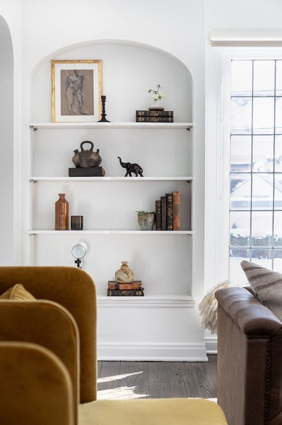 a large arched niche with shelves, with books, decor and artwork is a beautiful architectural feature for a living room