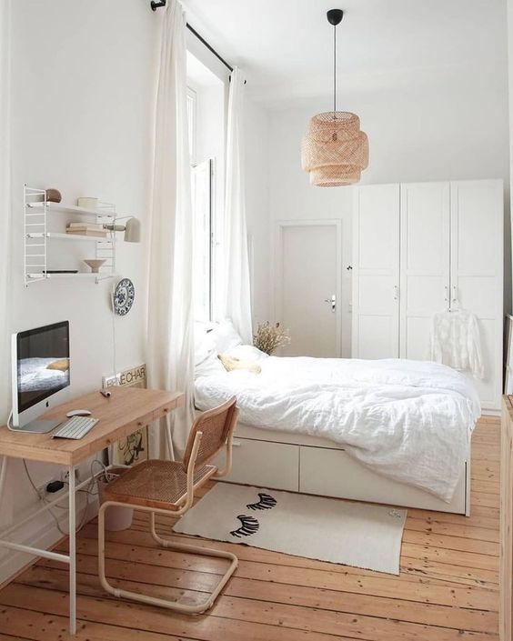 a neutral guest bedroom with a bed with storage, a wardrobe, a lightweight desk and a rattan chair, a woven pendant lamp