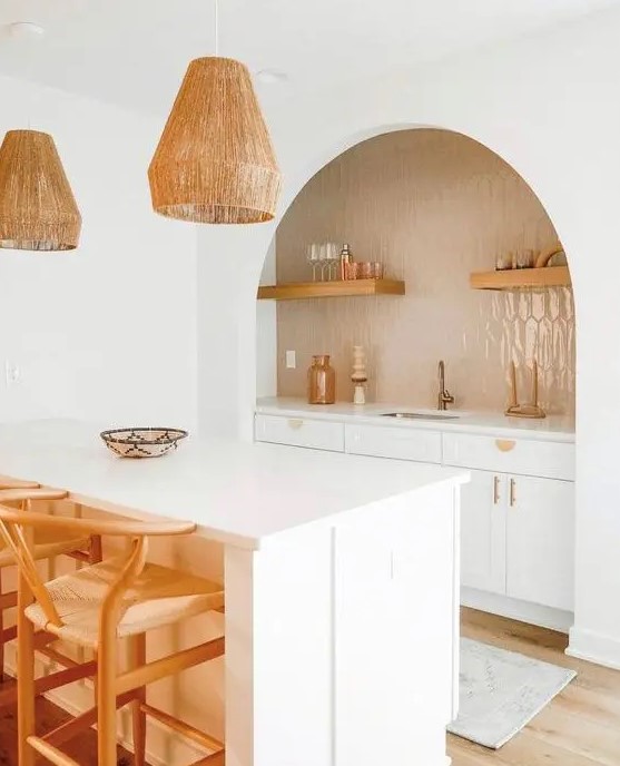 a lovely boho kitchen with white cabinets, an arched niche clad with tan tiles, open shelves, gold fixtures, pendant lamps