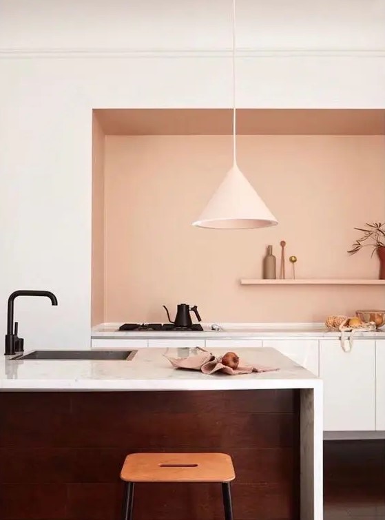 a modern kitchen with a large niche that is done with peachy paint and houses a row of cabinets and an open shelf, which is a super edgy solution