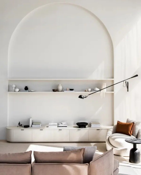 a minimalist living room in neutrals, with an arched niche with shelves for displaying stuff, a curved TV unit and some modern furniture