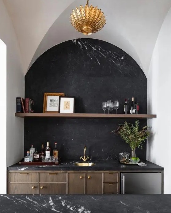 an exquisite kitchen with dark-stained cabinets and a kitchen island, black marble countertops and a backsplash, an arched niche that accommodates part of the cabinetry