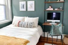 27 a dark green guest bedroom with a bed and neutral bedding, open shelves with a desk, a small chair and a gallery wall