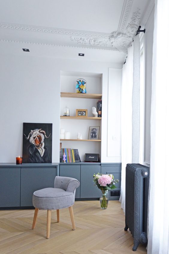 a modern living room with a niche with shelves, books and decor, graphite grey cabinets, a grey chair and some decor