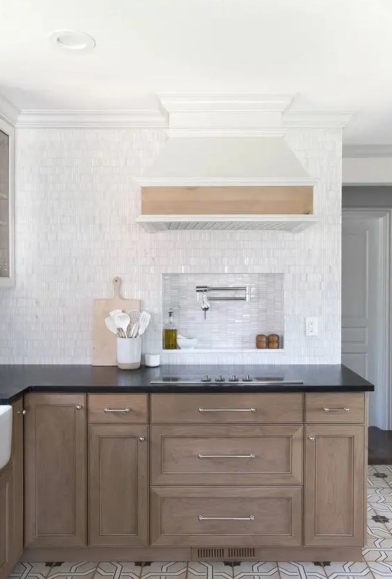 a farmhouse kitchen with stained cabinets, black countertops, white tiles with a niche over the cooker to store everything for cooking