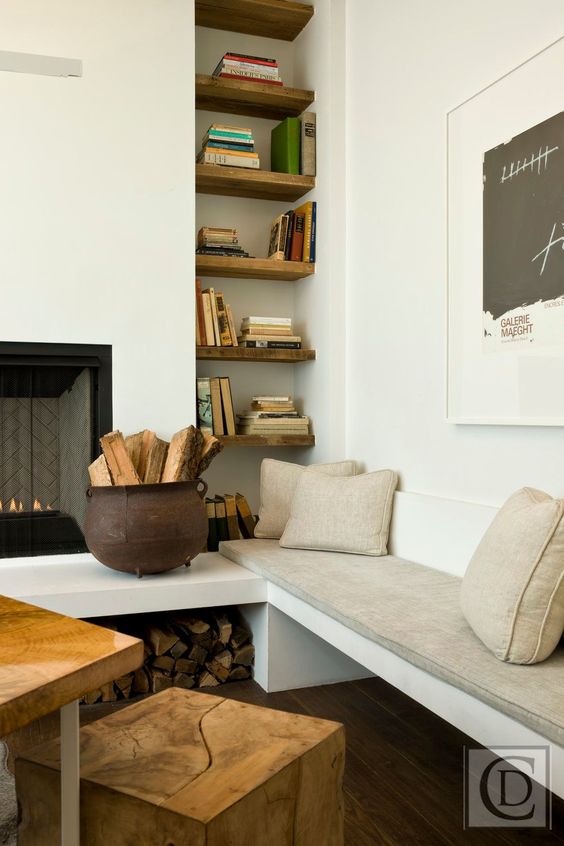 a neutral living room with a built-in fireplace and niche shelves, a corner bench with neutral upholstery and a table with a stool