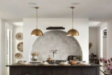 31 a modern kitchen with an arched niche clad with Zellige tiles and built-in cabinets, a black kitchen island, brass pendant lamps and industrial stools