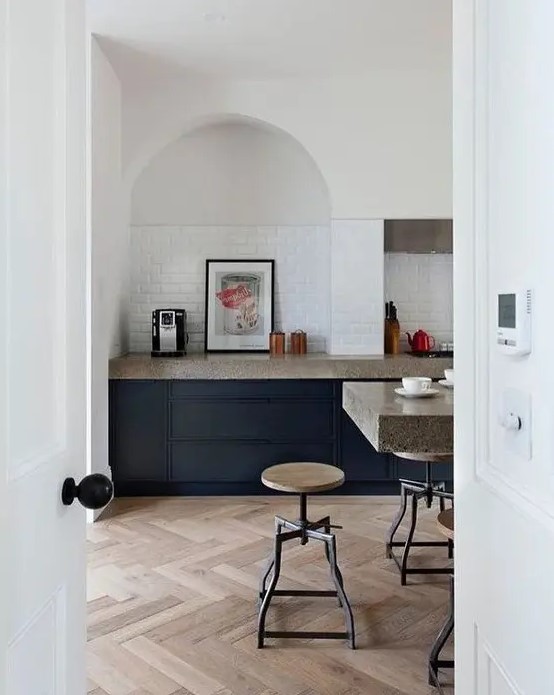 a modern kitchen with navy cabinets, grey granite countertops, an arched niche clad with tiles and artwork