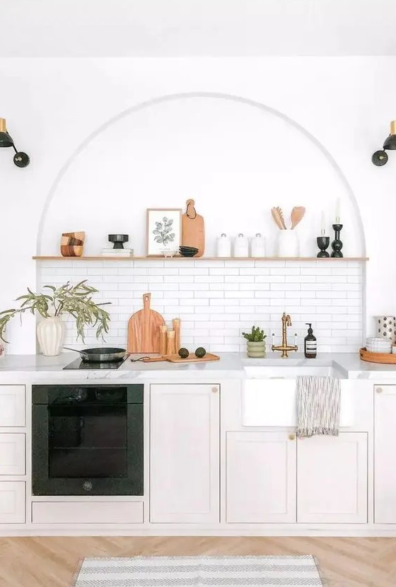 a modern kitchen with neutral lower cabinets, white marble countertops, an arched niche with a tile backsplash and an open shelf used for decor