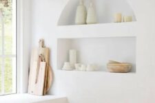 40 a serene white kitchen with lower cabinets, niche shelves used for decor and display and wooden cutting boards is a lovely space