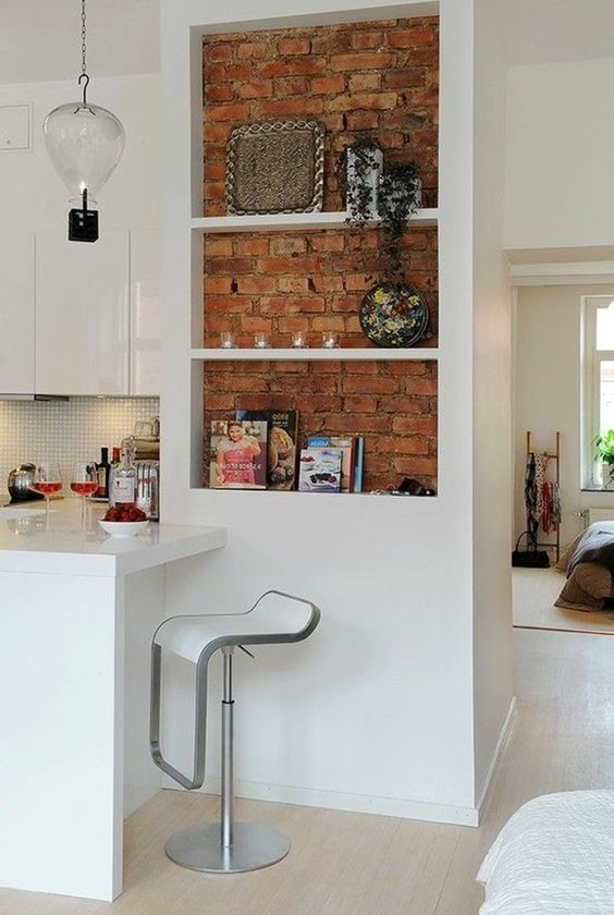 a sleek white kitchen with a niche done with red brick used for displaying some decor and potted greenery