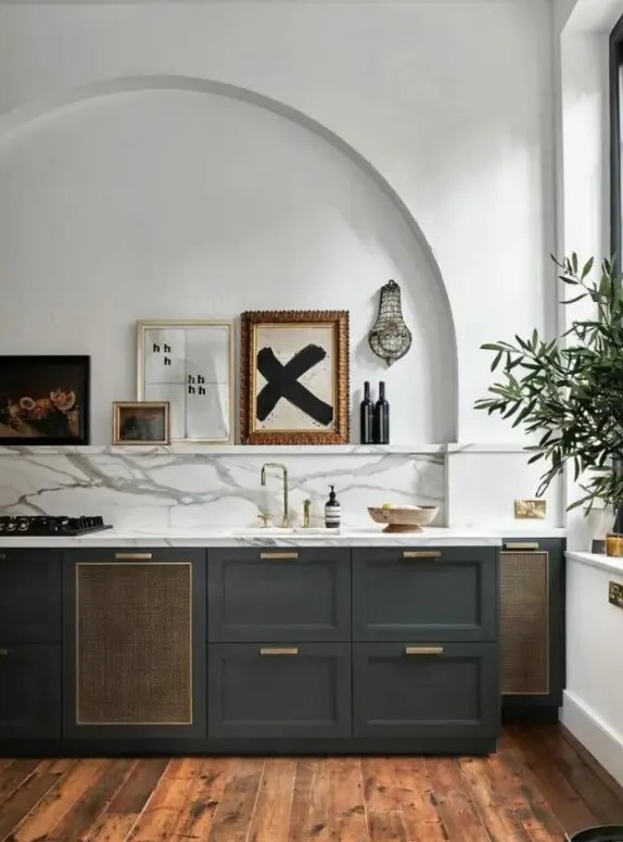 a stylish charcoal grey kitchen with a white marble backsplash and countertops, an arched niche with a ledge and a gallery wall in it